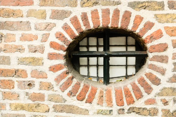 Oval, round window closed with cast-iron bars in fence bricked into old brick wall of a cellar, Utrecht, Netherlands. High quality photo