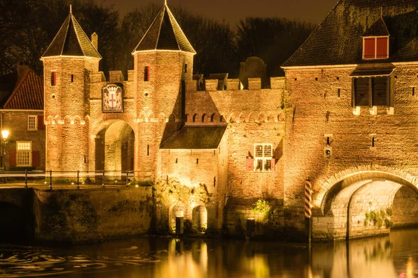 stock image Illuminated medieval monument De Koppelpoort, built in the 14th and 15th centuries, a brick gate with shutters bridging the river Eem at night, Amersfoort, the Netherlands. High quality photo, long