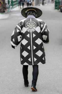 Sokakta yürürken görülen bir kişi, geleneksel Japon kıyafetleri giymiş, belirgin siyah beyaz geometrik desenli ve arkasında büyük dairesel bir amblem var. Aynı zamanda...