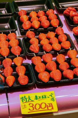 Çubukta taze çilek sergisi. Fiyatı 300 yen. Bu meyveler pembe bir yüzey üzerinde sunuluyor, bu da Japonya 'da bir pazar ortamının göstergesi..