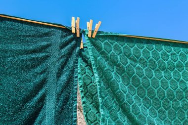 Açık mavi gökyüzüne karşı parlak güneş ışığında çamaşır ipinde kuruyan renkli havlular, yaz günü açık havada canlı bir atmosfer yaratıyor..