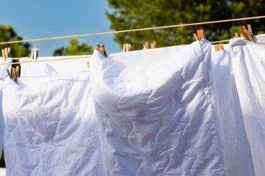 Açık mavi gökyüzüne karşı parlak güneş ışığında çamaşır ipinde kuruyan beyaz çamaşırlar, açık hava ortamında yaz günlerinde canlı bir atmosfer yaratıyor..