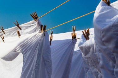 Açık mavi gökyüzüne karşı parlak güneş ışığında çamaşır ipinde kuruyan beyaz çamaşırlar, açık hava ortamında yaz günlerinde canlı bir atmosfer yaratıyor..