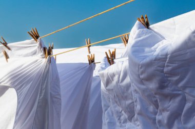 Açık mavi gökyüzüne karşı parlak güneş ışığında çamaşır ipinde kuruyan beyaz çamaşırlar, açık hava ortamında yaz günlerinde canlı bir atmosfer yaratıyor..