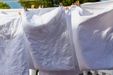 Açık mavi gökyüzüne karşı parlak güneş ışığında çamaşır ipinde kuruyan beyaz çamaşırlar, açık hava ortamında yaz günlerinde canlı bir atmosfer yaratıyor..