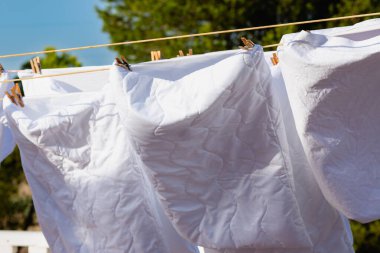 Açık mavi gökyüzüne karşı parlak güneş ışığında çamaşır ipinde kuruyan beyaz çamaşırlar, açık hava ortamında yaz günlerinde canlı bir atmosfer yaratıyor..