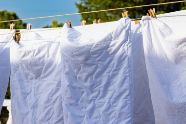 Açık mavi gökyüzüne karşı parlak güneş ışığında çamaşır ipinde kuruyan beyaz çamaşırlar, açık hava ortamında yaz günlerinde canlı bir atmosfer yaratıyor..