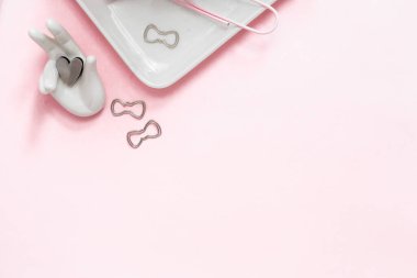 Beyaz ve gümüş kırtasiye aksesuarları içeren, açık pembe pastel arka plan çerçeveli kalemler ve boğa klipleri içeren ofis çalışma alanının kadınsı düz yatağı.