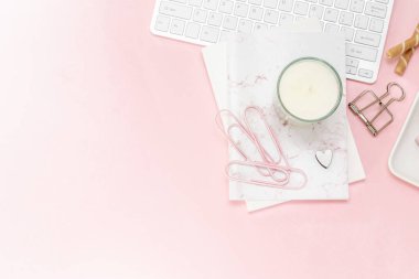 Feminen bir kadın çalışma alanı. Bilgisayarın gümüş klavyesi ve pastel pembe arka planda fotokopi alanı var. Mum ve diğer ofis alanı ve masaüstü beyaz kırtasiyeli resim