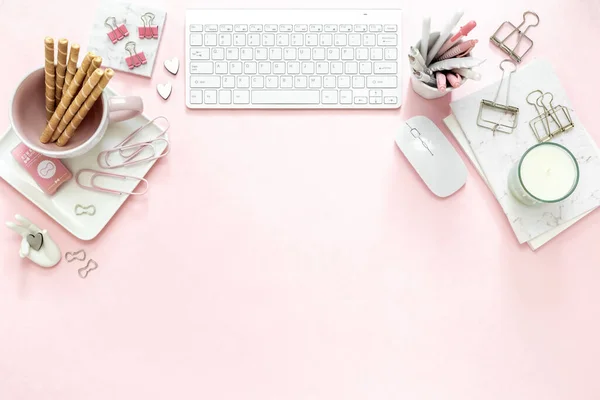 A feminine woman workspace, with a silver keyboard of a computer on a pastel pink background with copy space. Banner image with candle and other office space and desktop white stationery