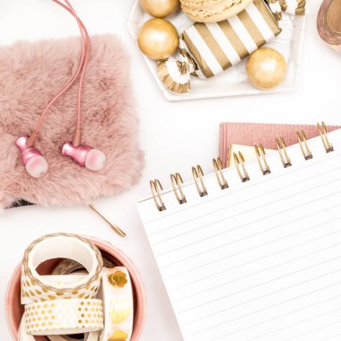 A femininely styled desktop in shades in gold and dusty pink with modem stationery. Lifestyle theme inspired by the office workspace of a stylish woman. Flat lay with fresh flowers pink keyboard and