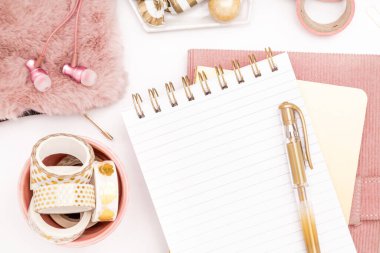 A femininely styled desktop in shades in gold and dusty pink with modem stationery. Lifestyle theme inspired by the office workspace of a stylish woman. Flat lay with fresh flowers pink keyboard and