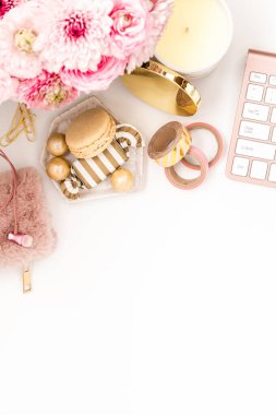 A femininely styled desktop in shades in gold and dusty pink with modem stationery. Lifestyle theme inspired by the office workspace of a stylish woman. Flat lay with fresh flowers pink keyboard and