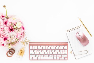 A femininely styled desktop in shades in gold and dusty pink with modem stationery. Lifestyle theme inspired by the office workspace of a stylish woman. Flat lay with fresh flowers pink keyboard and