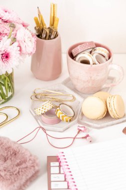 A femininely styled desktop in shades in gold and dusty pink with modem stationery. Lifestyle theme inspired by the office workspace of a stylish woman. With fresh flowers including Ranuculus
