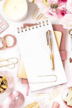 A femininely styled desktop in shades in gold and dusty pink with modem stationery. Lifestyle theme inspired by the office workspace of a stylish woman. Flat lay with fresh flowers pink keyboard and