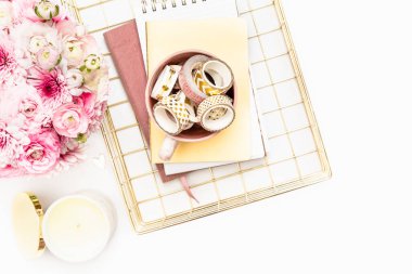 A femininely styled desktop in shades in gold and dusty pink with modem stationery. Lifestyle theme inspired by the office workspace of a stylish woman. With fresh flowers including Ranuculus