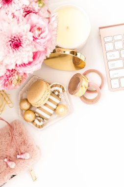 A femininely styled desktop in shades in gold and dusty pink with modem stationery. Lifestyle theme inspired by the office workspace of a stylish woman. Flat lay with fresh flowers pink keyboard and