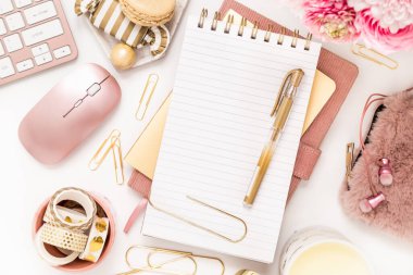 A femininely styled desktop in shades in gold and dusty pink with modem stationery. Lifestyle theme inspired by the office workspace of a stylish woman. Flat lay with fresh flowers pink keyboard and