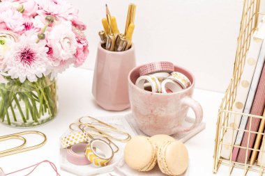 A femininely styled desktop in shades in gold and dusty pink with modem stationery. Lifestyle theme inspired by the office workspace of a stylish woman. Flat lay with fresh flowers pink keyboard and
