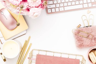 A femininely styled desktop in shades in gold and dusty pink with modem stationery. Lifestyle theme inspired by the office workspace of a stylish woman. Flat lay with fresh flowers pink keyboard and