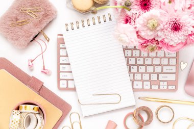 A femininely styled desktop in shades in gold and dusty pink with modem stationery. Lifestyle theme inspired by the office workspace of a stylish woman. Flat lay with fresh flowers pink keyboard and