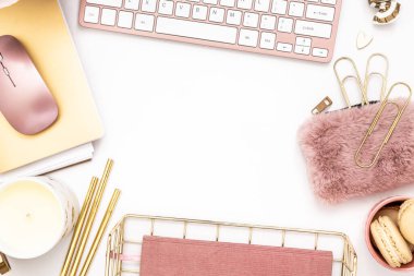 A femininely styled desktop in shades in gold and dusty pink with modem stationery. Lifestyle theme inspired by the office workspace of a stylish woman. Flat lay with fresh flowers pink keyboard and