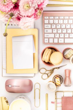 A femininely styled desktop in shades in gold and dusty pink with modem stationery. Lifestyle theme inspired by the office workspace of a stylish woman. Flat lay with fresh flowers pink keyboard and