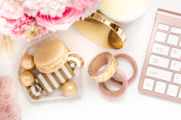 A femininely styled desktop in shades in gold and dusty pink with modem stationery. Lifestyle theme inspired by the office workspace of a stylish woman. Flat lay with fresh flowers pink keyboard and
