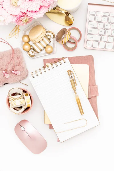 A femininely styled desktop in shades in gold and dusty pink with modem stationery. Lifestyle theme inspired by the office workspace of a stylish woman. Flat lay with fresh flowers pink keyboard and