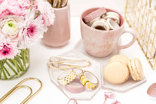 A femininely styled desktop in shades in gold and dusty pink with modem stationery. Lifestyle theme inspired by the office workspace of a stylish woman. With fresh flowers including Ranuculus