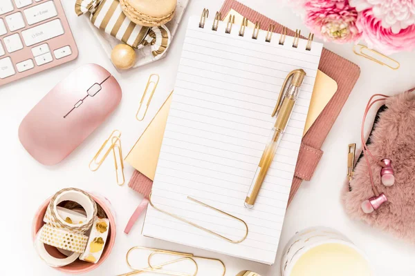 A femininely styled desktop in shades in gold and dusty pink with modem stationery. Lifestyle theme inspired by the office workspace of a stylish woman. Flat lay with fresh flowers pink keyboard and