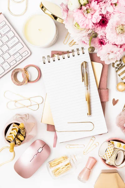 A femininely styled desktop in shades in gold and dusty pink with modem stationery. Lifestyle theme inspired by the office workspace of a stylish woman. Flat lay with fresh flowers pink keyboard and