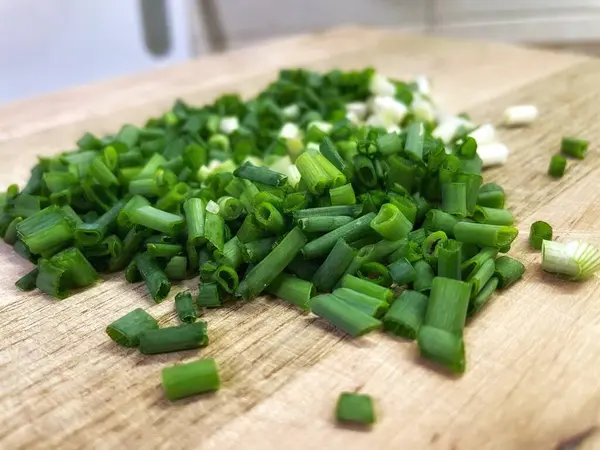 Doğranmış yeşil soğanlar, masanın üzerindeki tahta kesme tahtasının üzerinde. Mutfakta, yemek, yemek, yemek.