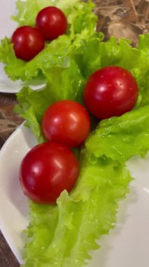 Yemek, vitaminler, yeşil marul yaprakları ve kırmızı domatesler bir tabakta yatıyor.