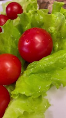 Yemek, vitaminler, yeşil marul yaprakları ve kırmızı domatesler bir tabakta yatıyor.