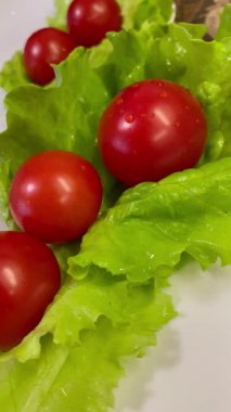 Yemek, vitaminler, yeşil marul yaprakları ve kırmızı domatesler bir tabakta yatıyor.