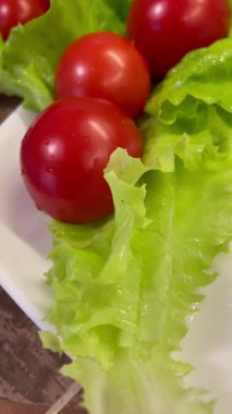 Yemek, vitaminler, yeşil marul yaprakları ve kırmızı domatesler bir tabakta yatıyor.