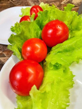 Yemek, vitaminler, yeşil marul yaprakları ve kırmızı domatesler bir tabakta yatıyor.