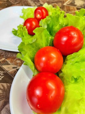 Yemek, vitaminler, yeşil marul yaprakları ve kırmızı domatesler bir tabakta yatıyor.