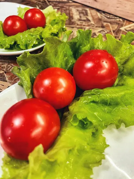 Yemek, vitaminler, yeşil marul yaprakları ve kırmızı domatesler bir tabakta yatıyor.