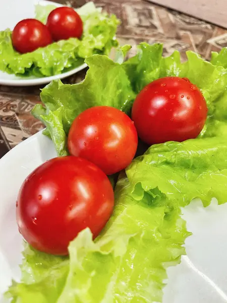 Yemek, vitaminler, yeşil marul yaprakları ve kırmızı domatesler bir tabakta yatıyor.