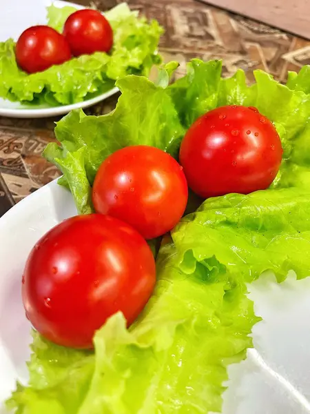 Yemek, vitaminler, yeşil marul yaprakları ve kırmızı domatesler bir tabakta yatıyor.