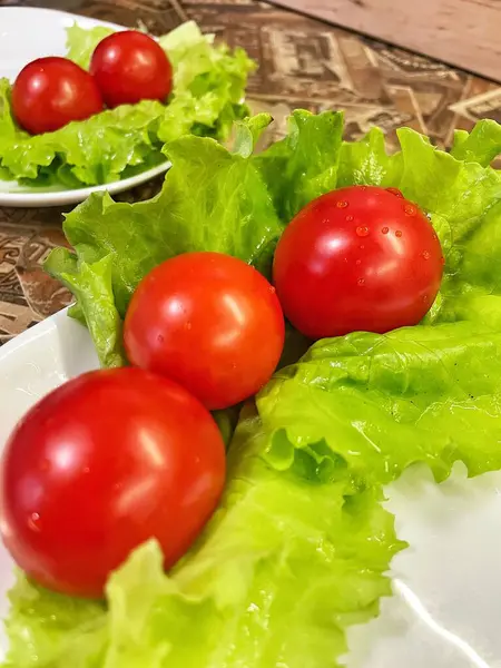 Yemek, vitaminler, yeşil marul yaprakları ve kırmızı domatesler bir tabakta yatıyor.