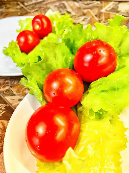 Yemek, vitaminler, yeşil marul yaprakları ve kırmızı domatesler bir tabakta yatıyor.