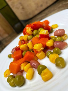 Beyaz tabakta parlak renkli sebzeler: mısır, bezelye, fasulye, biber, havuç, sağlığa iyi gelir, yemek pişirme