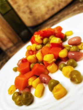 Beyaz tabakta parlak renkli sebzeler: mısır, bezelye, fasulye, biber, havuç, sağlığa iyi gelir, yemek pişirme