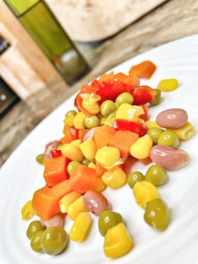 Beyaz tabakta parlak renkli sebzeler: mısır, bezelye, fasulye, biber, havuç, sağlığa iyi gelir, yemek pişirme