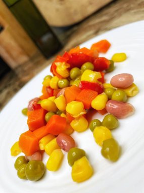 Beyaz tabakta parlak renkli sebzeler: mısır, bezelye, fasulye, biber, havuç, sağlığa iyi gelir, yemek pişirme