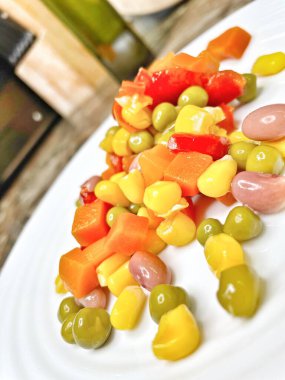 Beyaz tabakta parlak renkli sebzeler: mısır, bezelye, fasulye, biber, havuç, sağlığa iyi gelir, yemek pişirme